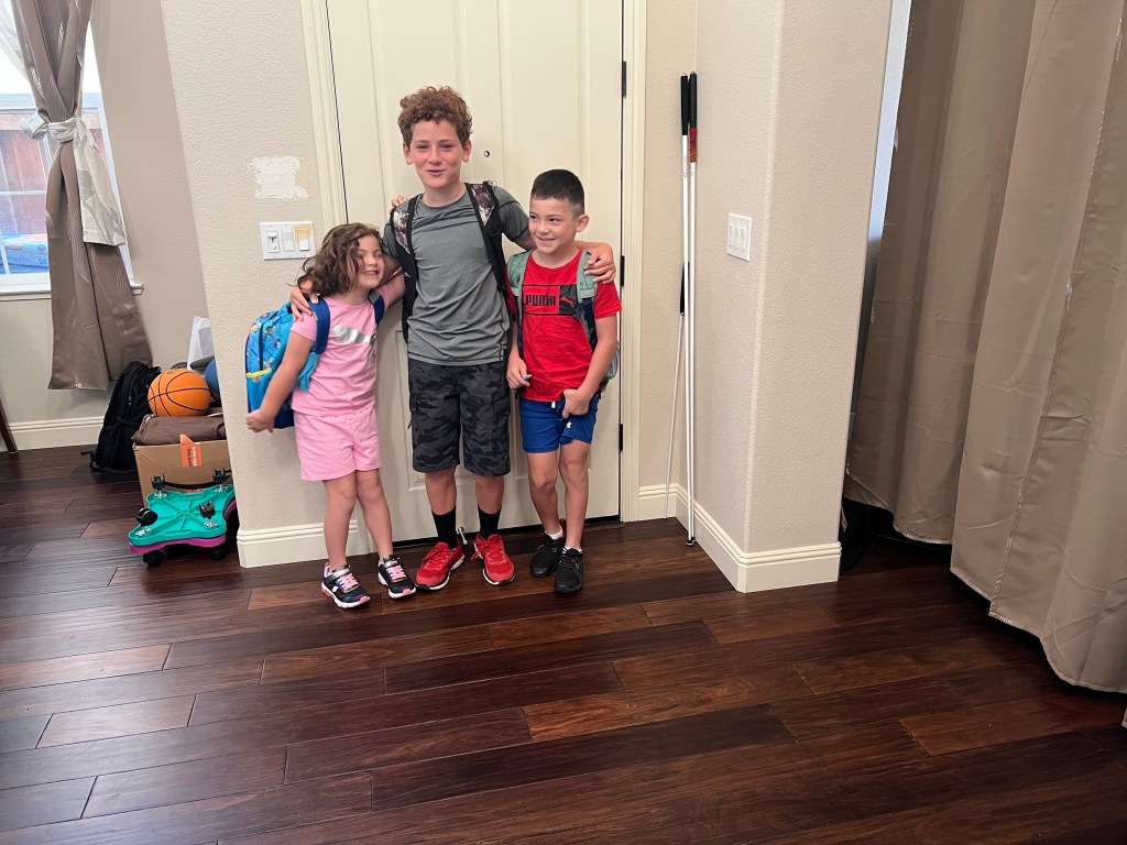 From left to right: MacKenzy is wearing all pink. Erik is wearing a dark gray shirt with black shorts, black socks, and red shoes. Zakary is wearing a red shirt and blue shorts.￼